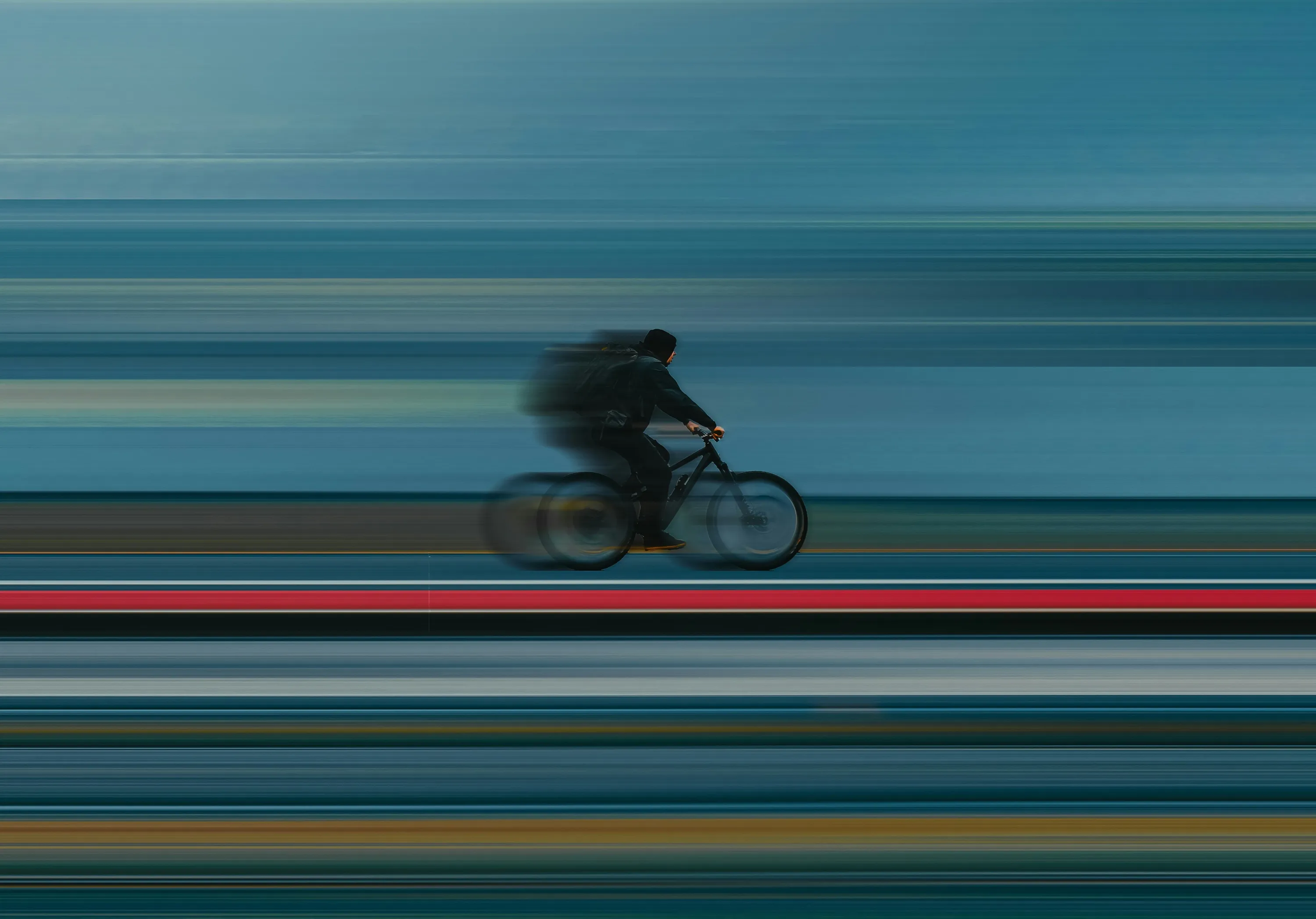 A cyclist in sharp focus speeding past a background blurred into horizontal bands of blue, with one red stripe along the road